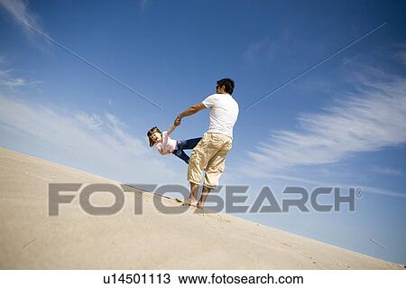 Stock Image - Man swings girl (4) in circle, Grand Beach Provincial Park, Manitoba, Canada. Fotosearch