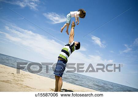 Stock Photograph - Man throws girl (4) up into air, Grand Beach Provincial Park, Manitoba, Canada. Fotosearch
