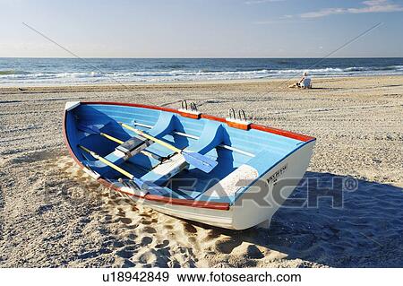Stock Photo - Mature man sitting on beach and small boat, New Jersy, USA.. Fotosearch