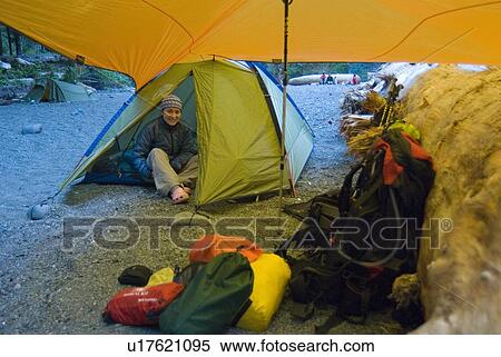 Stock Photography - Woman (20-25) in a tent under a tarp while camping on a hiking trip, West Coast Trail, Pacific Rim National Park Reserve, BC, Canada. Fotosearch