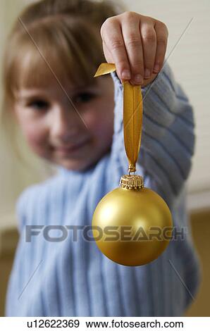 Stock Photo - Girl holding gold Christmas ornament. Fotosearch