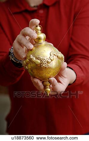 Stock Image - Woman holding gold Christmas ornament. Fotosearch