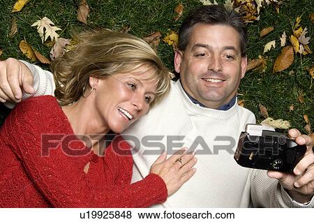 Stock Photo - Couple taking their own photo while lying in fall leaves. Fotosearch