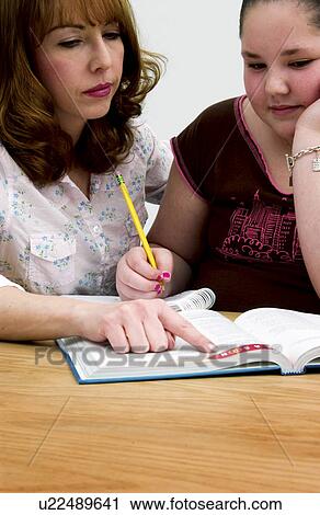 Stock Image - Mother or teacher helping girl with homework. Fotosearch