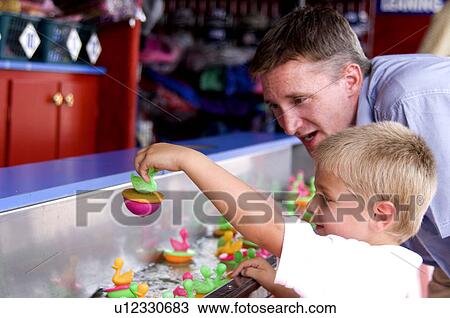 Stock Image - Father and son playing carnival game. Fotosearch