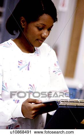 Stock Image - African American nurse looking at patient chart. Fotosearch