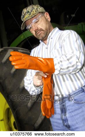 Stock Photograph - Man putting on orange rubber safety gloves. Fotosearch
