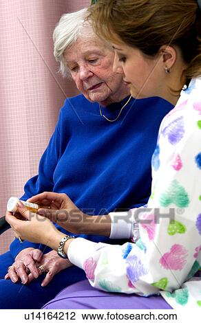 Stock Image - Nurse giving senior woman a bottle of pills. Fotosearch