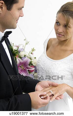 Stock Photo - Groom putting ring on bride's finger. Fotosearch