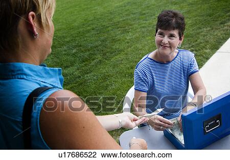Stock Image - Woman collecting money at garage sale. Fotosearch