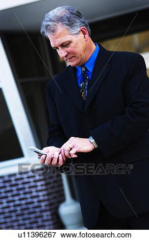 Businessman in front of building dialing a cell phone View Large Photo Image Stock Photo - Businessman in front of building dialing a cell phone. Fotosearch