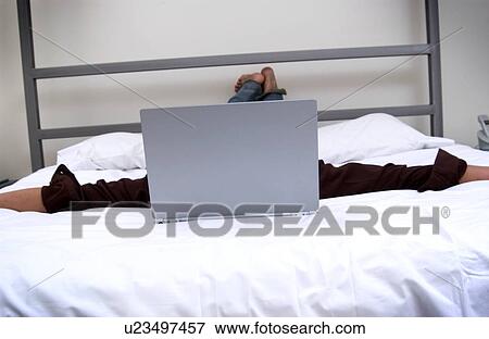 Man working on laptop computer while lying on bed View Large Photo Image Stock Photo - Man working on laptop computer while lying on bed. Fotosearch