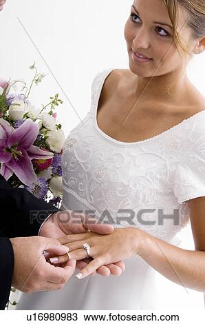 Stock Image - Groom putting ring on bride's finger. Fotosearch