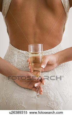 Stock Photography - Woman holding glass of champagne behind her back. Fotosearch