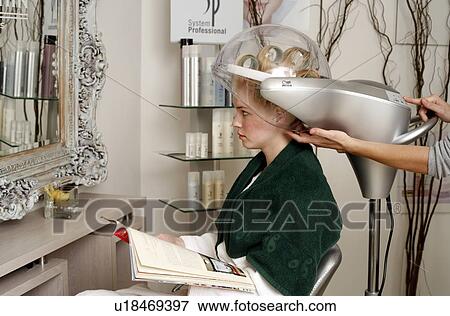 Stock Photo - Young woman sitting under hairdryer. Fotosearch