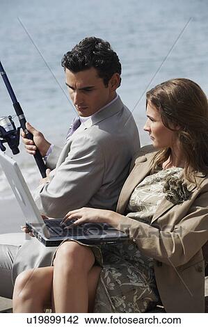 Stock Image - Business couple on beach with fishing rod and laptop. Fotosearch