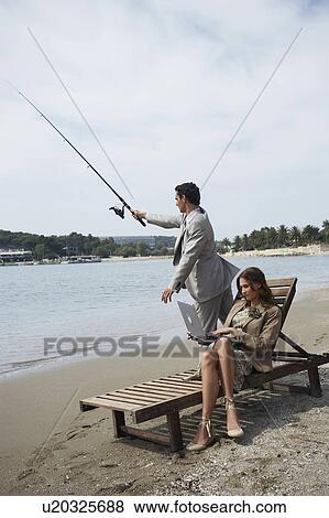 Stock Photo - Business couple on beach with fishing rod and laptop. Fotosearch