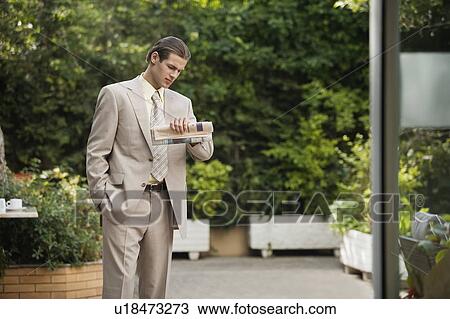 Stock Image - Businessman in garden looking at watch. Fotosearch