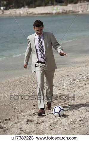 Stock Image - Businessman on beach playing soccer. Fotosearch