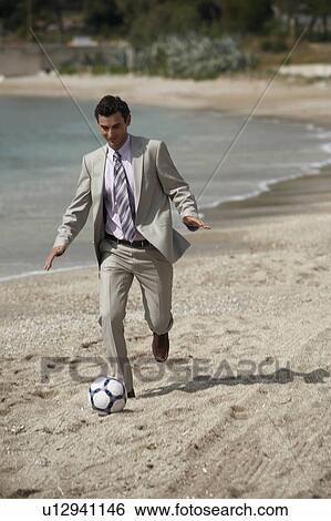 Stock Photograph - Businessman on beach playing soccer. Fotosearch