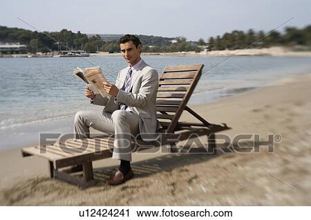 Stock Image - Businessman on beach with a newspaper. Fotosearch