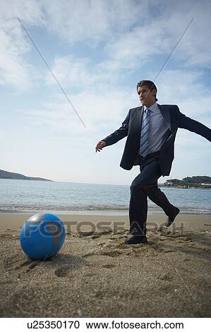 Stock Image - Businessman on beach with globe beach ball. Fotosearch