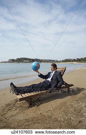 Stock Image - Businessman on chaise lounge with globe. Fotosearch