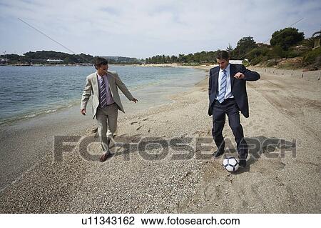 Stock Image - Businessmen on beach playing soccer. Fotosearch