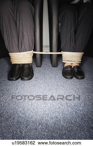Stock Image - Male and female business people's legs tied. Fotosearch