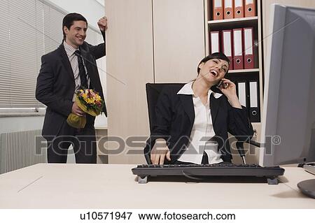 Male office worker about to surprise female colleague with flowers View Large Photo Image Stock Photo - Male office worker about to surprise female colleague with flowers. Fotosearch