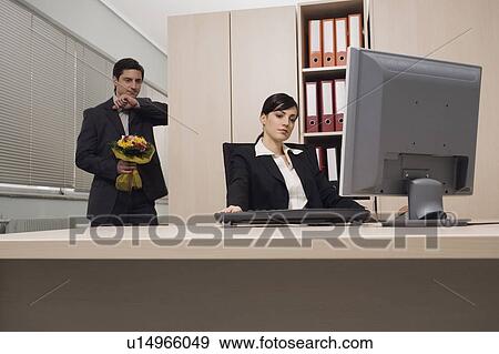 Stock Photo - Male office worker about to surprise female colleague with flowers. Fotosearch