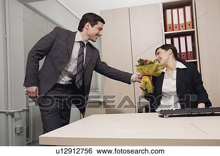 Stock Photograph - Male office worker giving flowers to female colleague. Fotosearch
