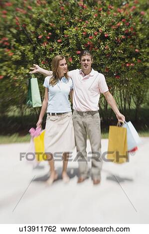 Stock Image - Couple in a park with shopping bags. Fotosearch