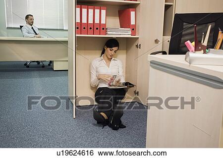 Employee reading magazine hiding from manager View Large Photo Image Stock Photograph - Employee reading magazine hiding from manager. Fotosearch
