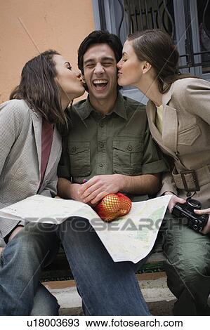 Stock Image - Man on bench being kissed by two women. Fotosearch