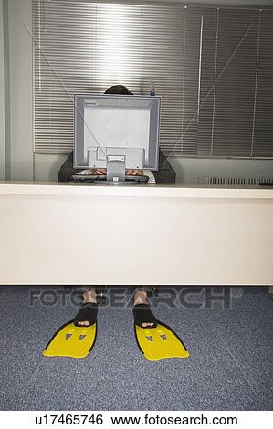 Stock Photograph - Office worker at computer wearing swim flippers. Fotosearch