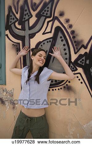 Stock Photo - Woman at wall with graffiti, arms up. Fotosearch