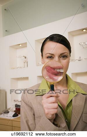 Stock Image - Woman with magnifying glass on mouth with tongue sticking out. Fotosearch