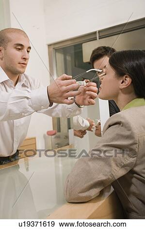 Optometrist adjusting glasses for woman in a store View Large Photo Image Stock Photo - Optometrist adjusting glasses for woman in a store. Fotosearch