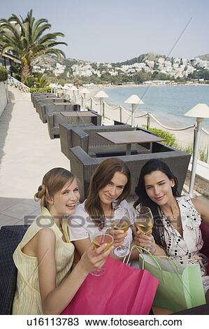 Stock Image - Three women with shopping bags toasting. Fotosearch