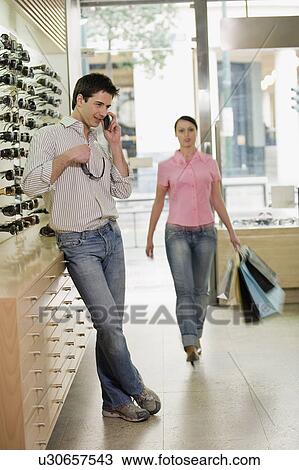 Stock Image - Woman entering sunglasses store with man on cell phone. Fotosearch