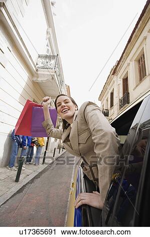 Stock Image - Woman leaning out of car with shopping bags. Fotosearch