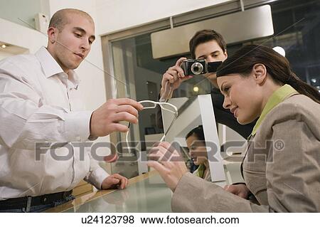 Stock Photo - Woman looking at glasses in store while man photographs. Fotosearch