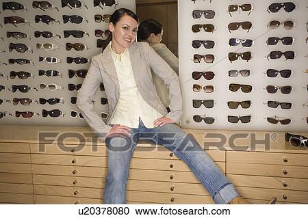 Stock Image - Woman posing in front of sunglasses display. Fotosearch