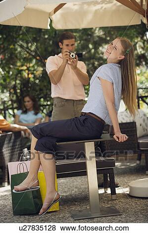 Stock Photo - Woman posing with shopping bags for man photographing her. Fotosearch