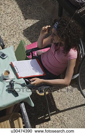 Stock Image - Woman sitting at a cafe with paper, pen, and shopping bags. Fotosearch
