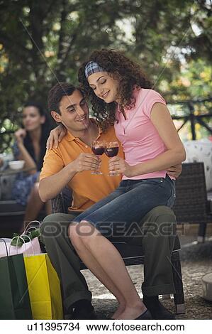 Picture - Woman sitting on man's lap with shopping bags in cafe. Fotosearch