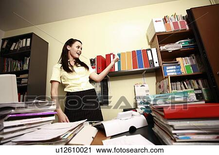 Stock Image - Female office worker in cluttered office. Fotosearch