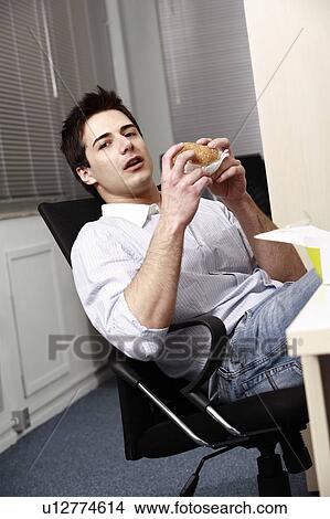 Office worker eating hamburger at desk View Large Photo Image Picture - Office worker eating hamburger at desk. Fotosearch