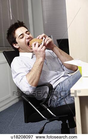 Office worker eating hamburger at desk View Large Photo Image Stock Photo - Office worker eating hamburger at desk. Fotosearch